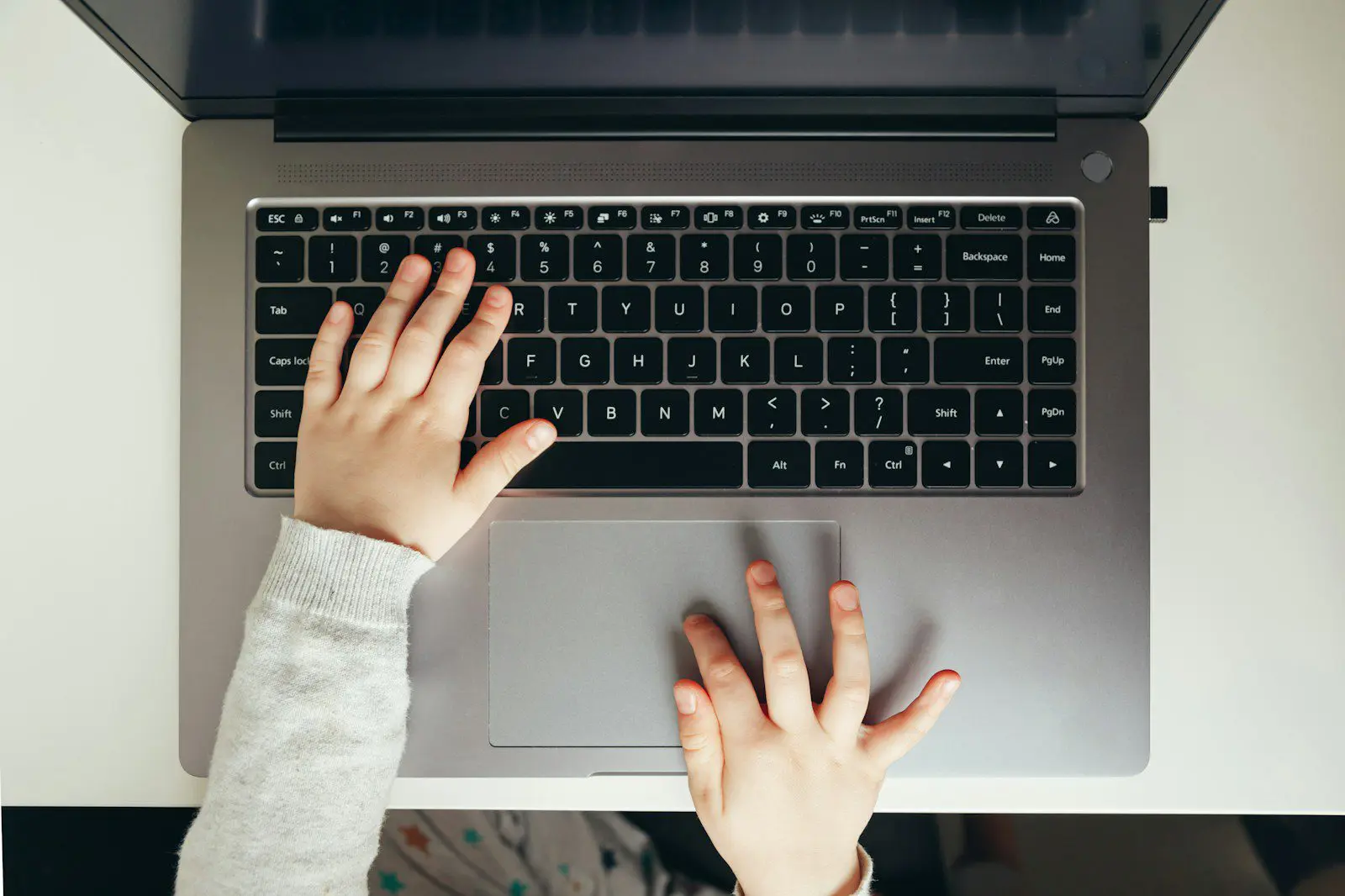 Child's hands typing on a laptop keyboard.