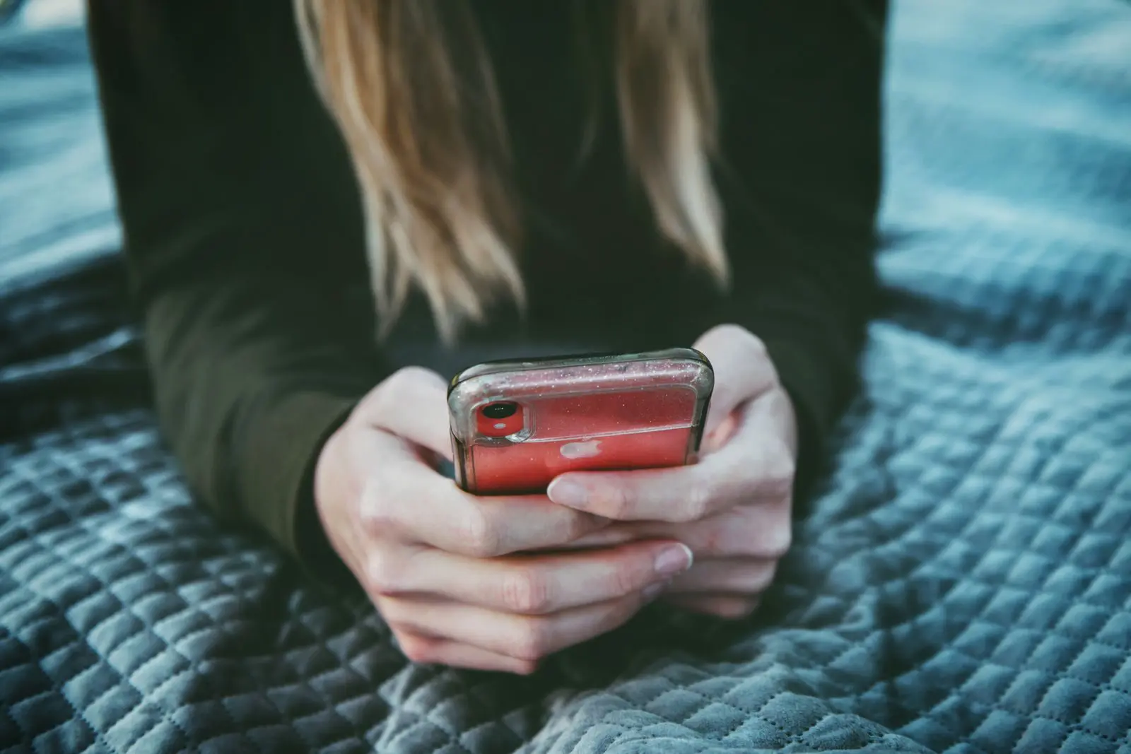 Close-up of a woman using a smartphone while sitting on a quilted blanket outdoors.